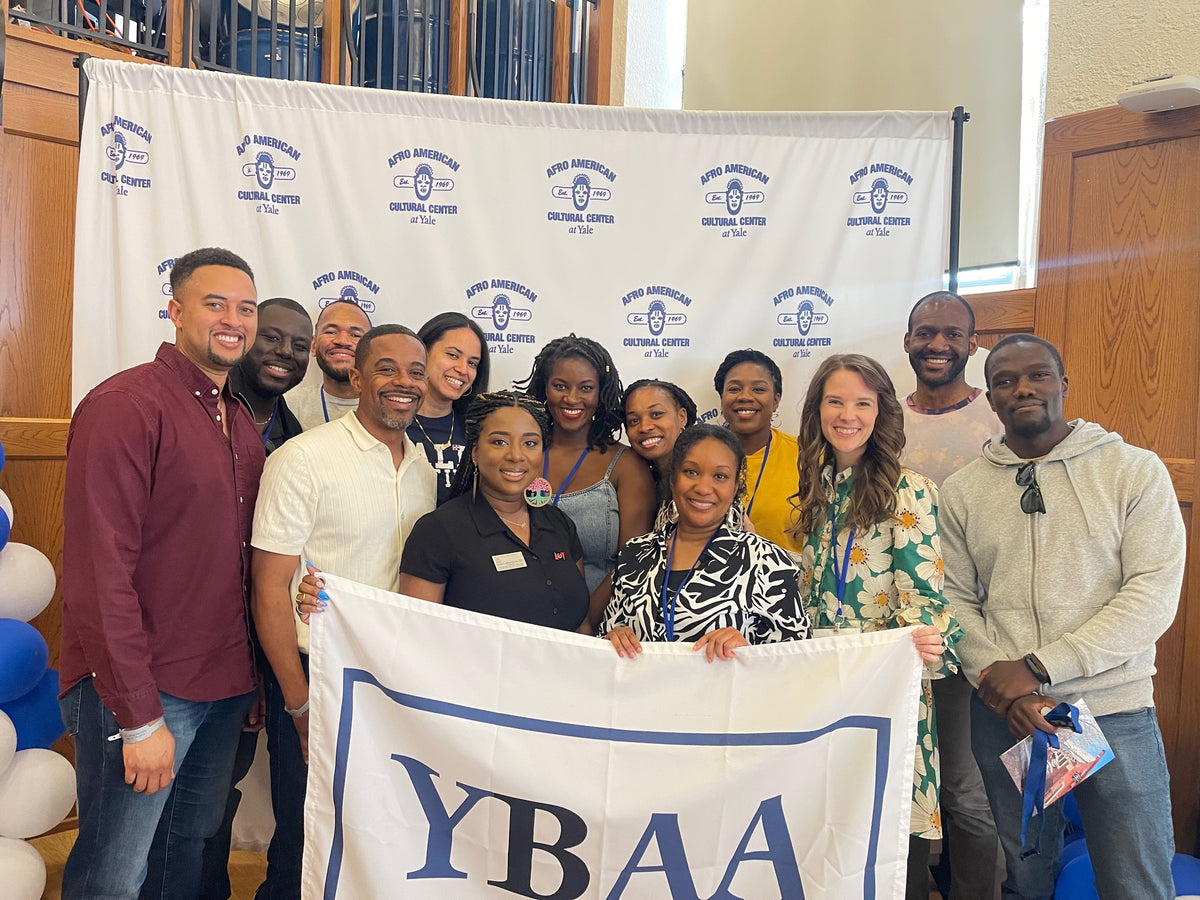 YBAA alumni holding a YBAA banner in front of an Afro-American Cultural Center at Yale backdrop